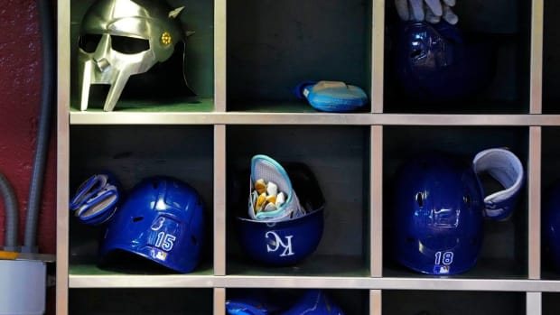 A bunch of Royals helmets sit in their cubbies in a dugout during a game.